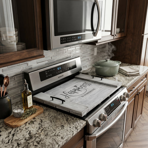 A rustic decorative wooden noodle board with distressed gray wood panels and black metal handles on the sides show in a kitchen setting. The center features the phrase 'Happiness is Homemade' in black lettering, with a small heart above the 'i' in 'Happiness'.